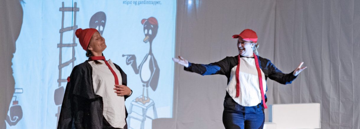 To damer er kledd ut som pingvinar. Står på ei scene.