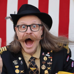 Ein mann med hatt, briller og stor bart